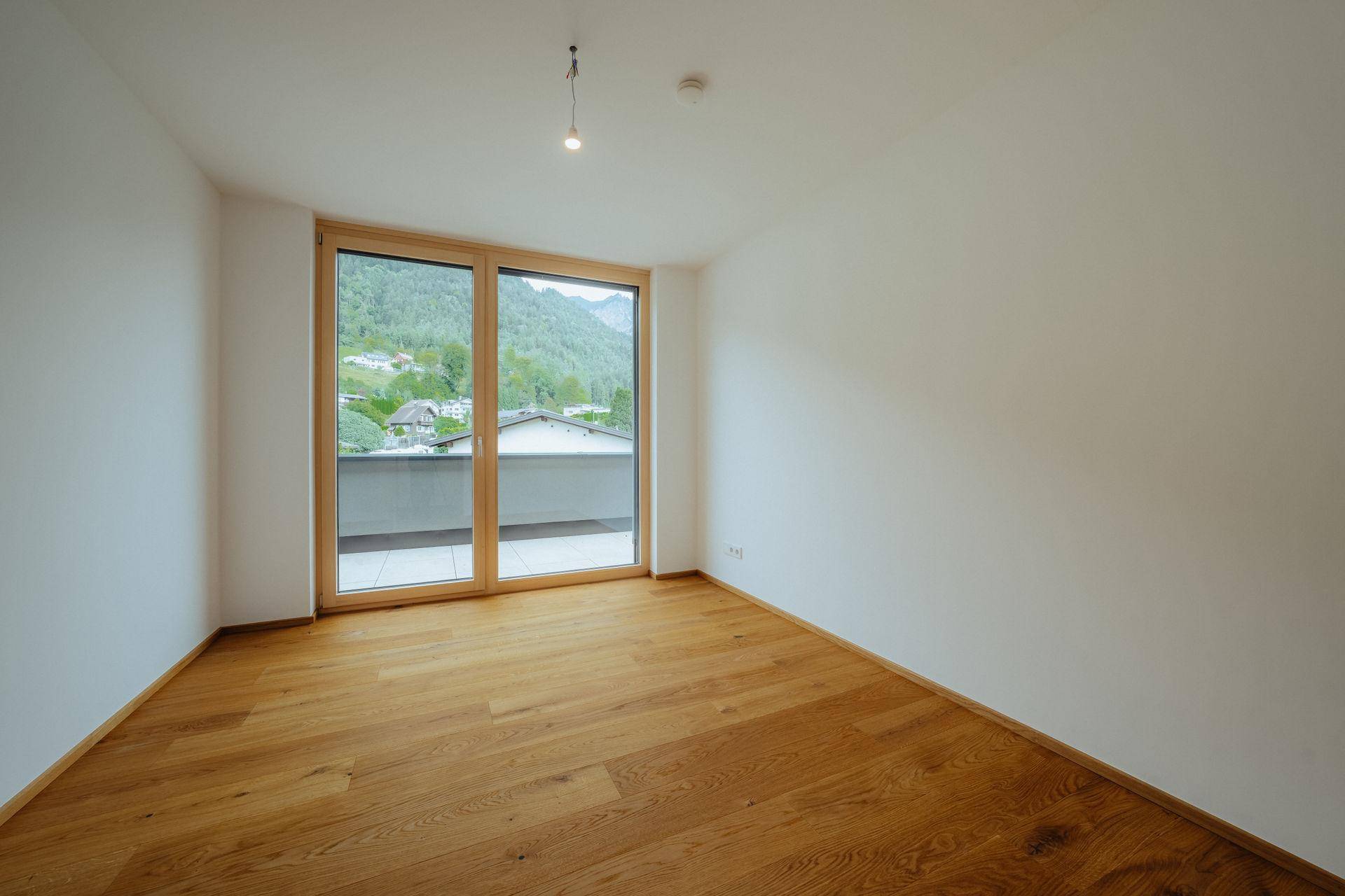 Helles Schlafzimmer mit Holzboden und Balkonzugang, bietet einen schönen Blick auf die grüne Berglandschaft.