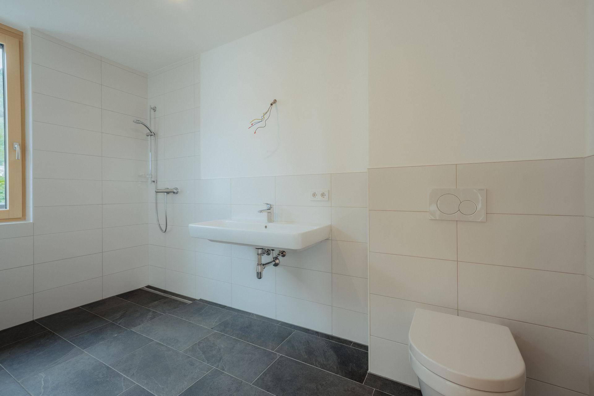 Modernes Badezimmer mit weißen Wandfliesen, dunklem Boden, wandhängendem Waschbecken und Duschbereich.