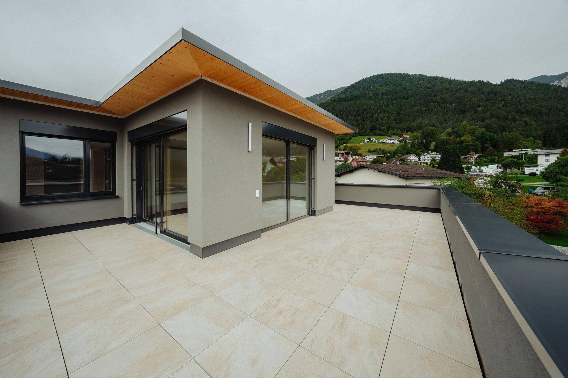 Großzügige Dachterrasse mit hellen Fliesen und Panoramablick auf die umliegende Berglandschaft.