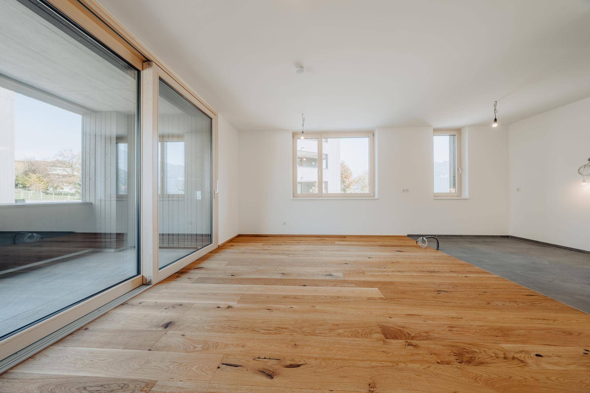 Geräumiges Wohnzimmer mit hellem Holzdielenboden und großen Schiebetüren, die viel Tageslicht hereinlassen.