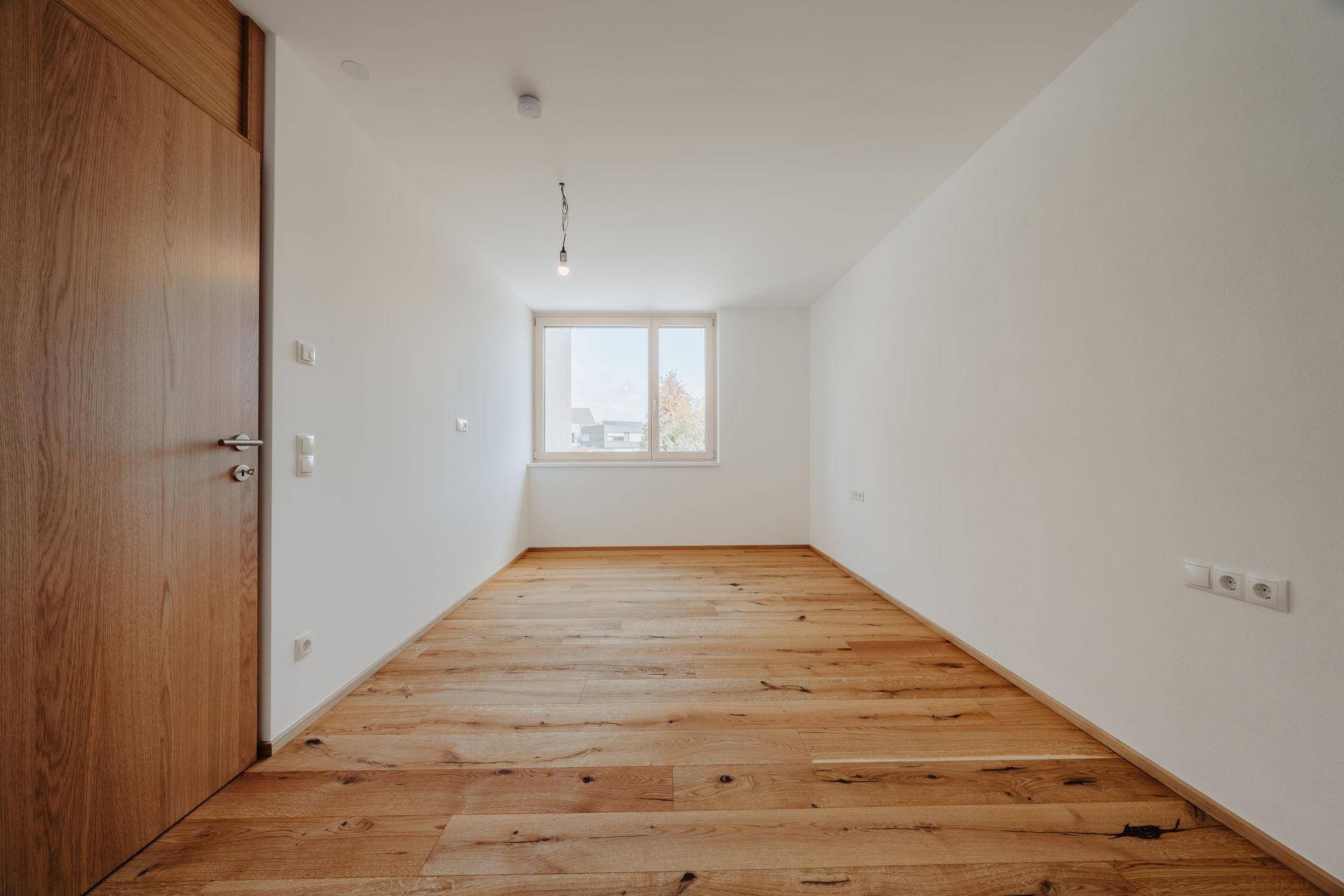 Helles, leeres Zimmer mit Holzdielenboden und weiß gestrichenen Wänden, ideal als Schlaf- oder Arbeitszimmer.