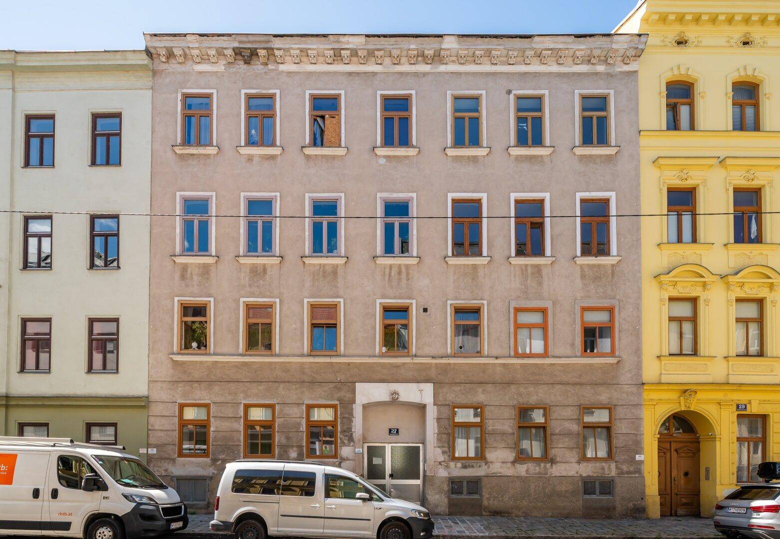 Historische Fassade eines Mehrfamilienhauses mit vielen Fenstern an einem sonnigen Tag.