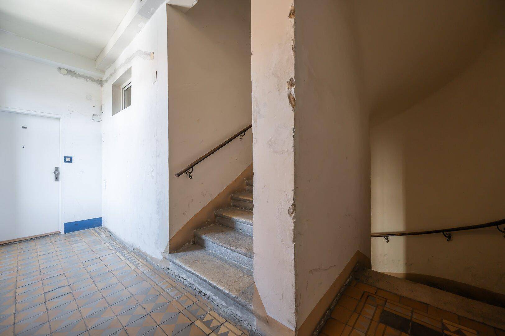 Treppenhaus mit gefliestem Boden und Handlauf, das zu den oberen Etagen führt.