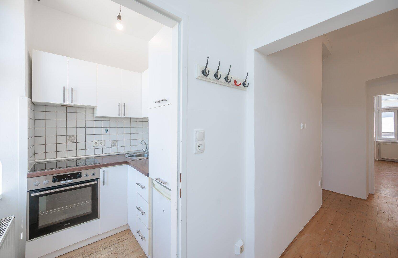 Kleine, funktionale Küche mit weißen Schränken, Fliesen und integriertem Backofen.