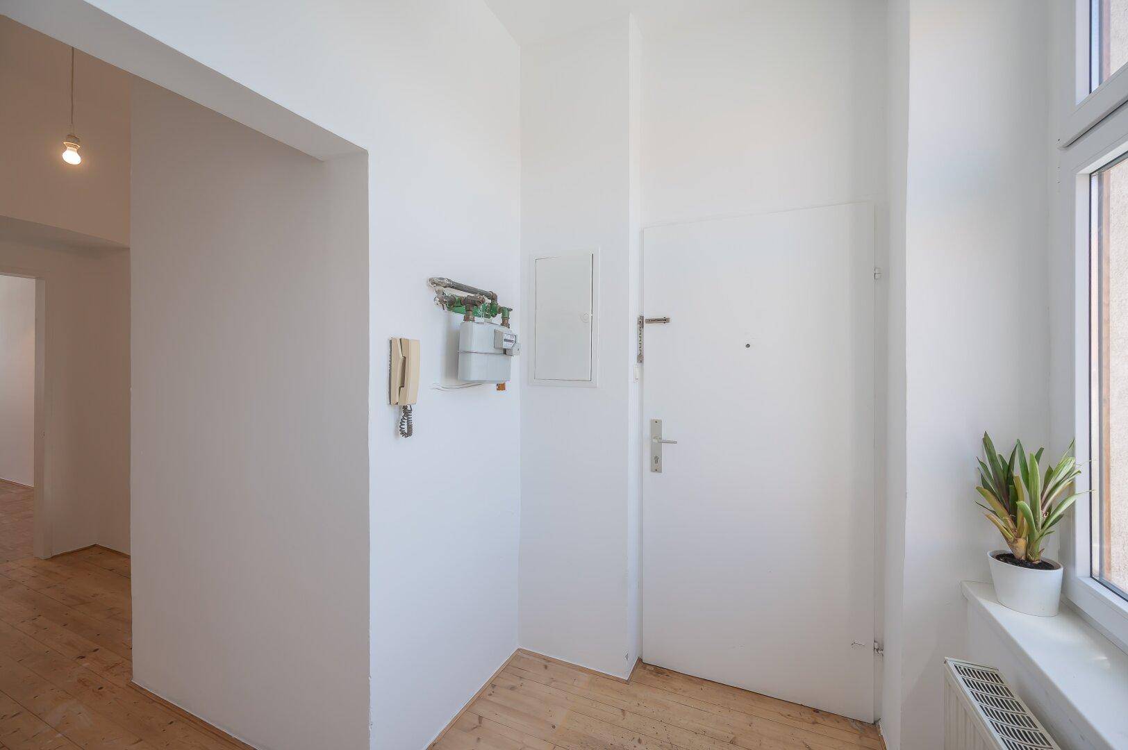 Heller Eingangsbereich mit Holzboden, Gegensprechanlage und Fenster.