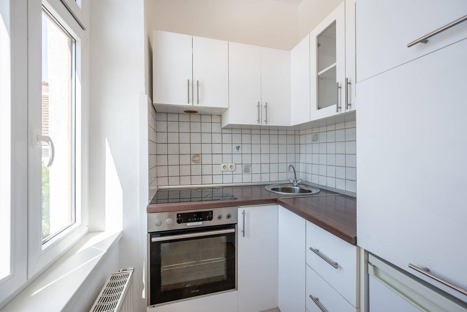 Kompakte Einbauküche mit weißen Fronten, Spüle und Kochfeld unter dem Fenster.