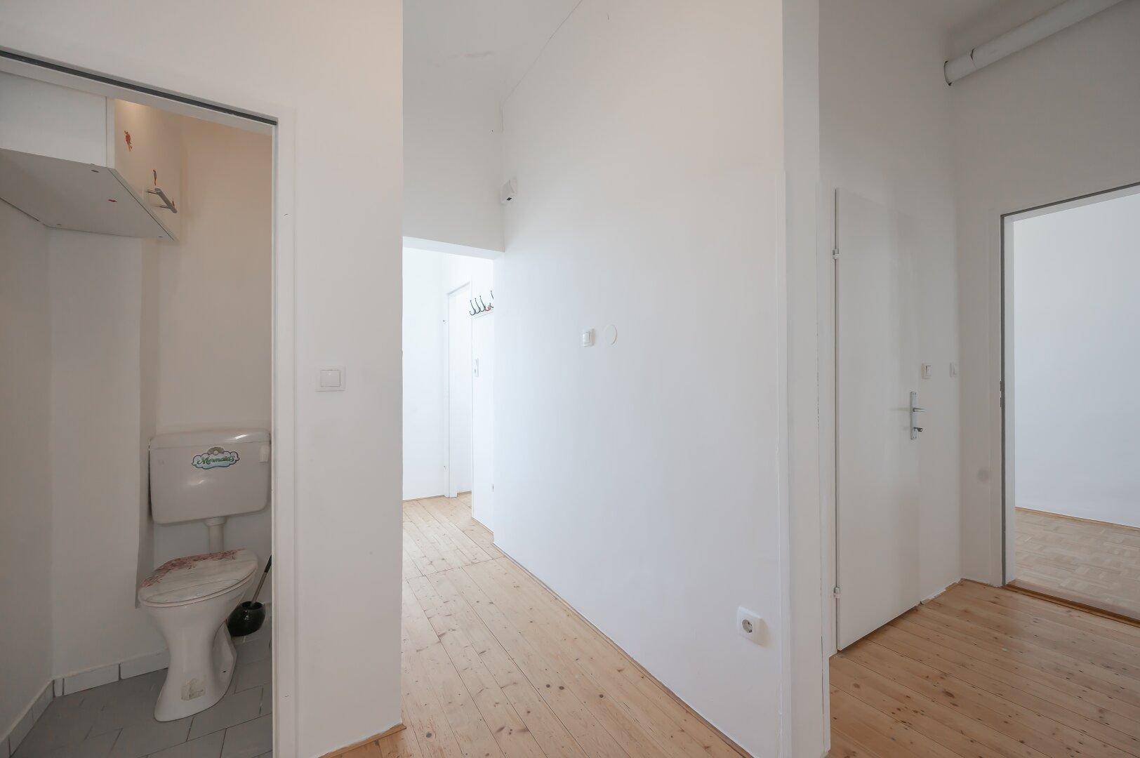 Langer Flur mit Holzboden und Zugang zu einem separaten WC-Bereich.