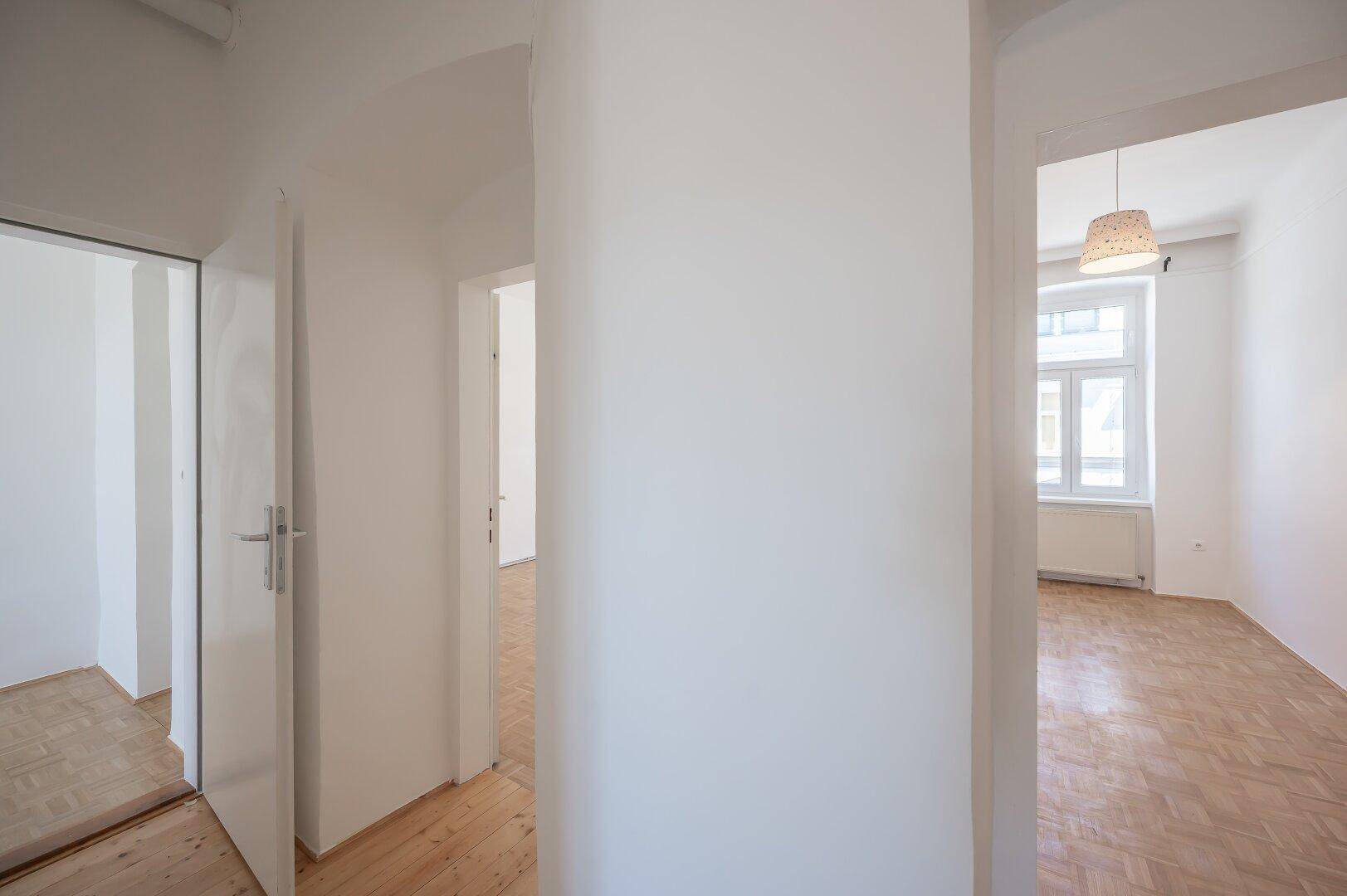 Heller Flur mit Holzboden, der zu verschiedenen Zimmern der Wohnung führt.