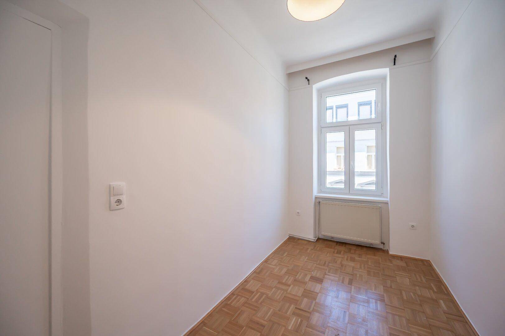 Helles Schlafzimmer mit Parkettboden und einem großen Fenster.