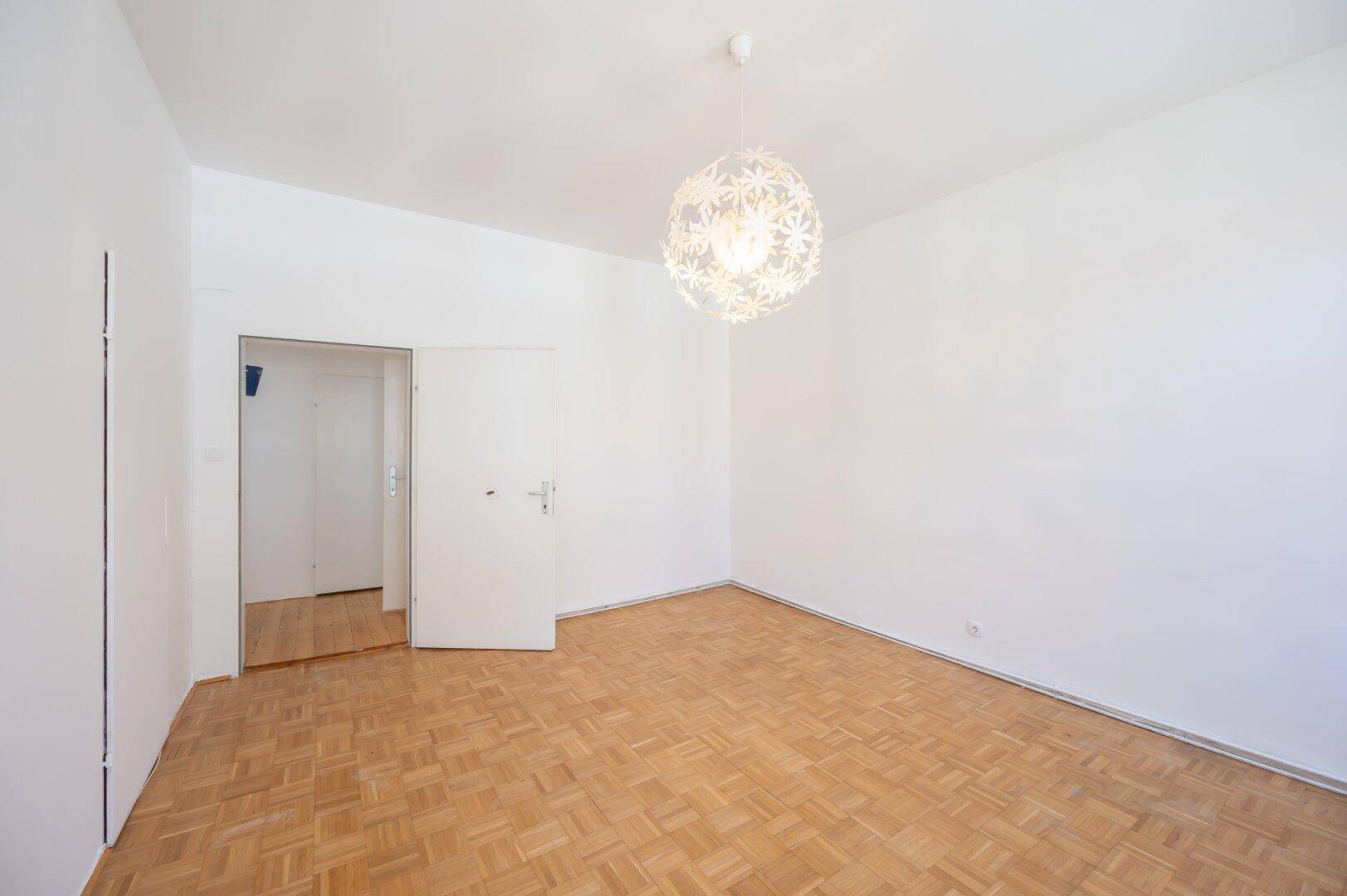 Geräumiges Zimmer mit Parkettboden und moderner Deckenleuchte, bereit zur Einrichtung.