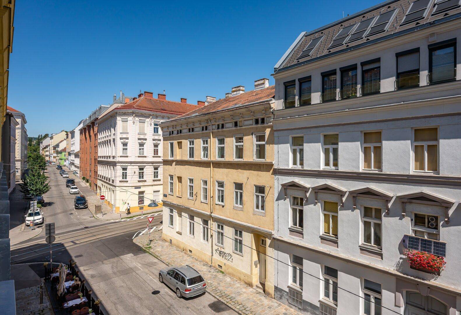Blick von oben auf eine belebte Stadtstraße mit historischen Gebäuden und parkenden Autos.