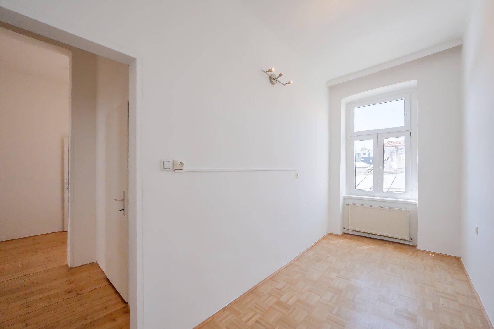 Helles Zimmer mit Parkettboden und einem Fenster, ideal als Schlaf- oder Arbeitszimmer.