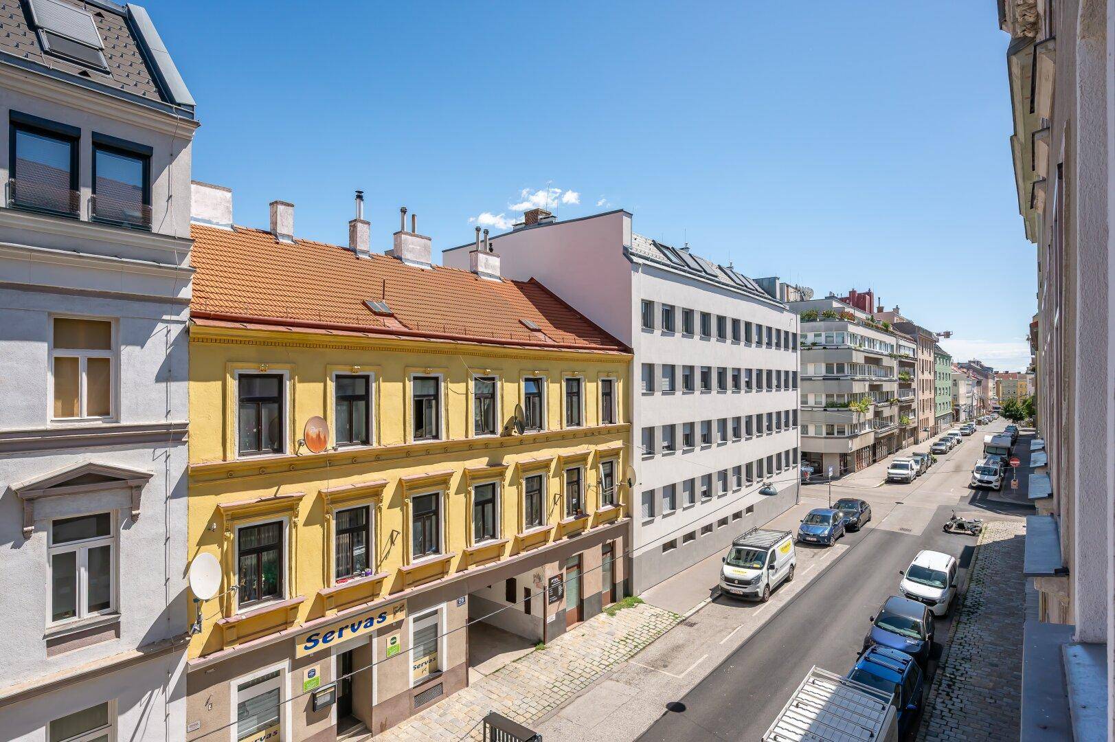 Panoramablick auf eine städtische Straße mit verschiedenen Gebäudefassaden und Fahrzeugen.