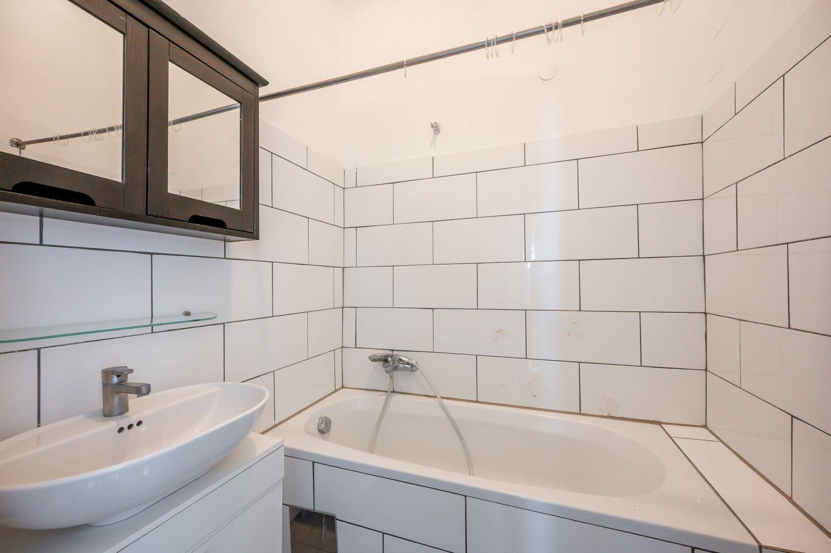 Badezimmer mit weißen Fliesen, Badewanne und modernem Waschbecken.