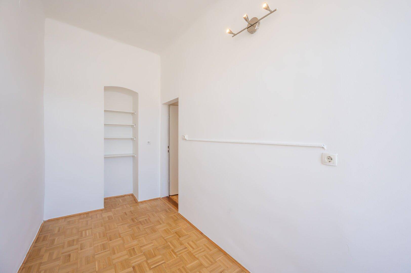 Helles Zimmer mit Parkettboden und praktischem Einbauregal.