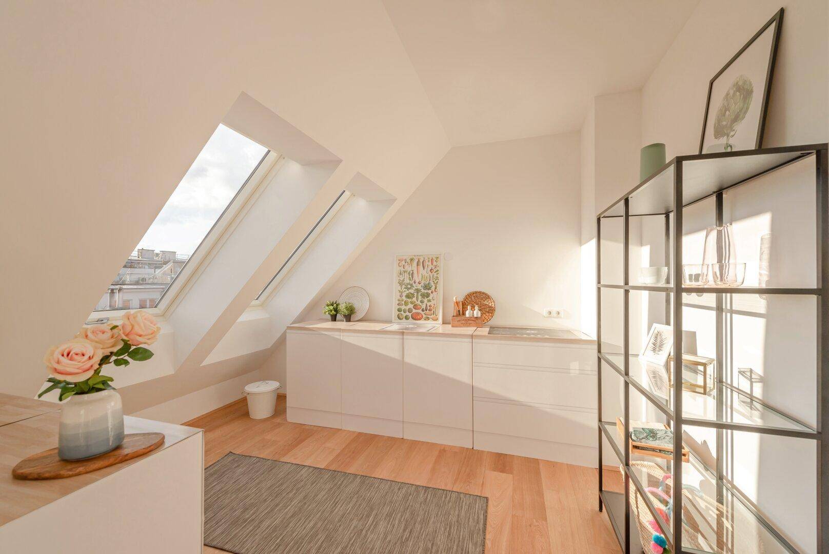 Kleine, moderne Küchenzeile im Dachgeschoss mit weißen Schränken und Dachfenstern, sonnendurchflutet.