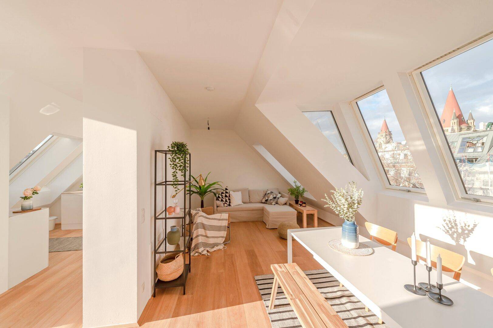 Sonniger Wohn- und Essbereich im Dachgeschoss mit Holzboden, Dachfenstern und Stadtblick.