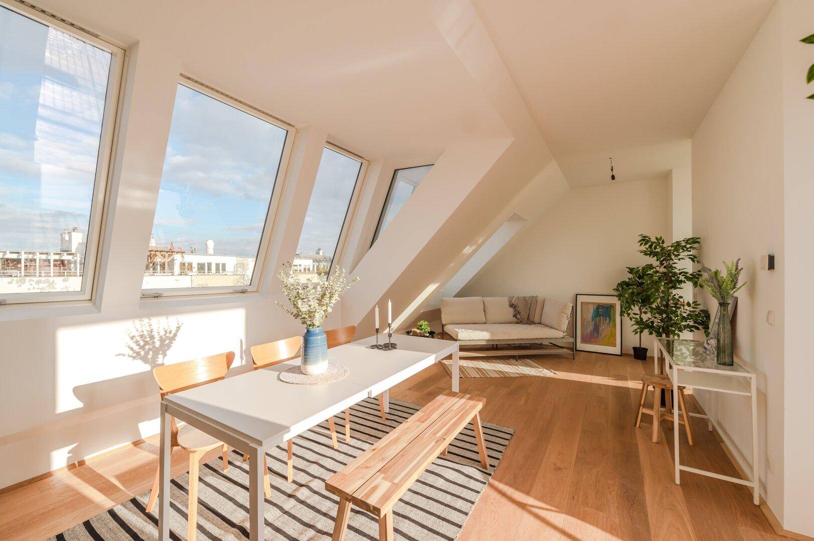Sonniger Wohn- und Essbereich im Dachgeschoss mit Holzboden, Dachfenstern und Stadtblick.