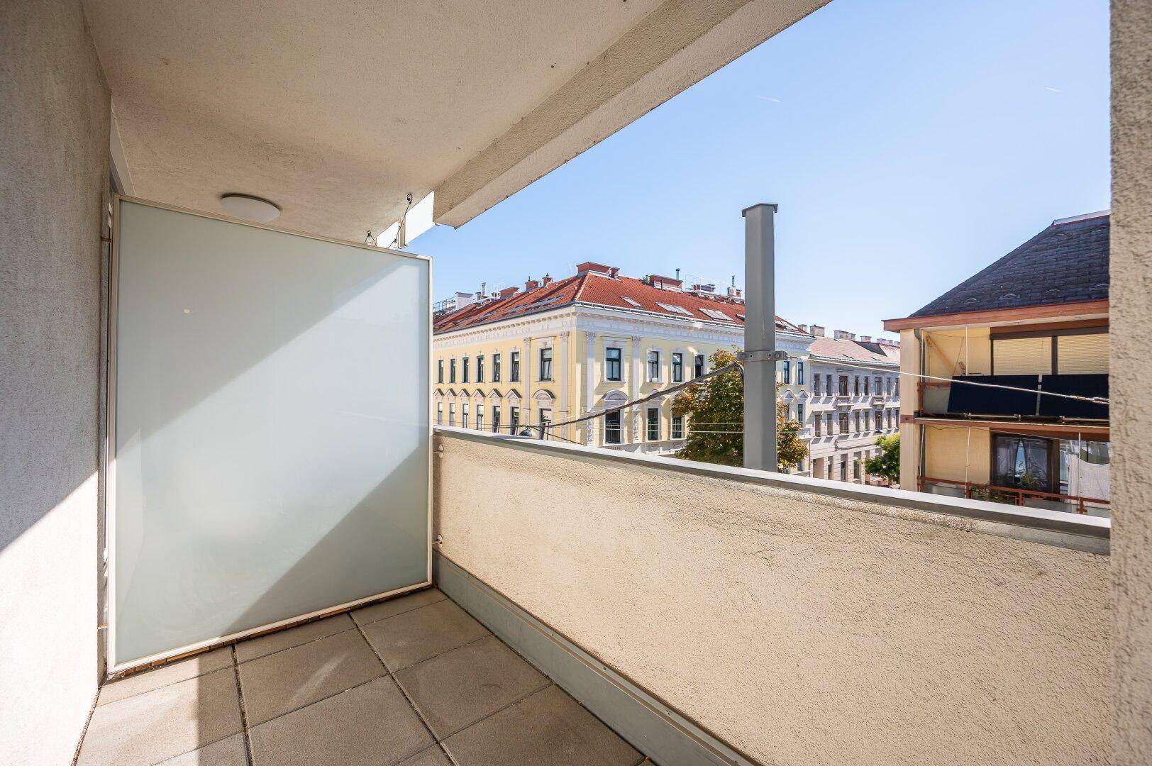 Sonniger Balkon mit Fliesenboden und Blick auf die umliegenden Gebäude der Stadt.