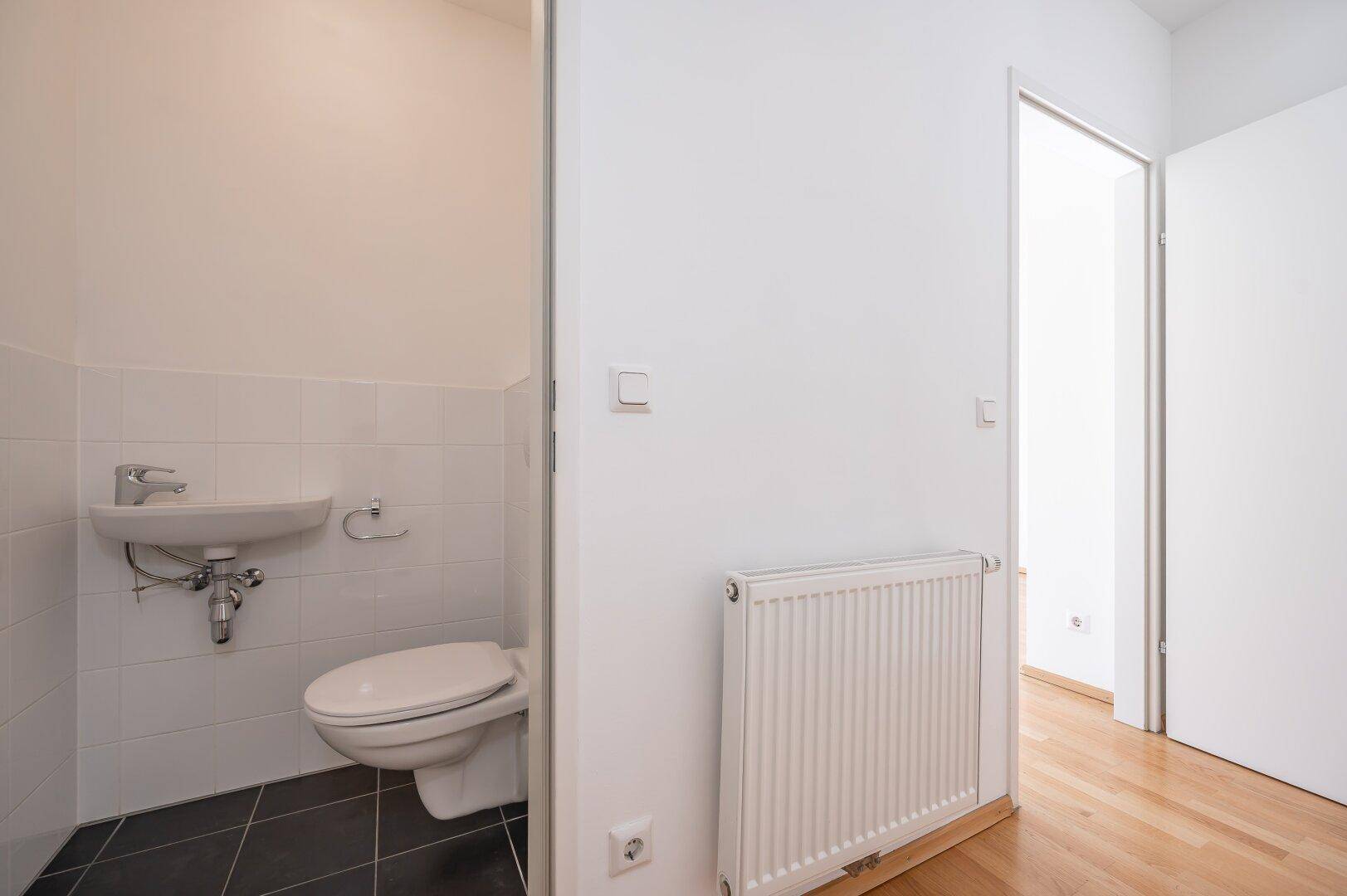 Separates Gäste-WC mit kleinem Waschbecken und dunklen Bodenfliesen, praktisch und funktional.