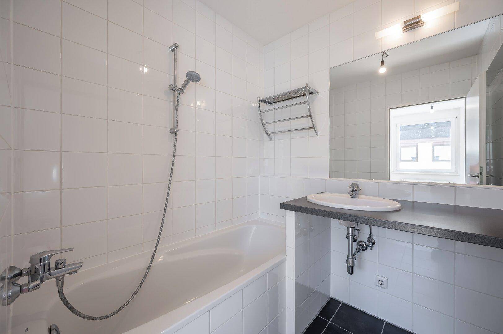 Modernes Badezimmer mit Badewanne, Duschfunktion und Waschbecken, hell gefliest.