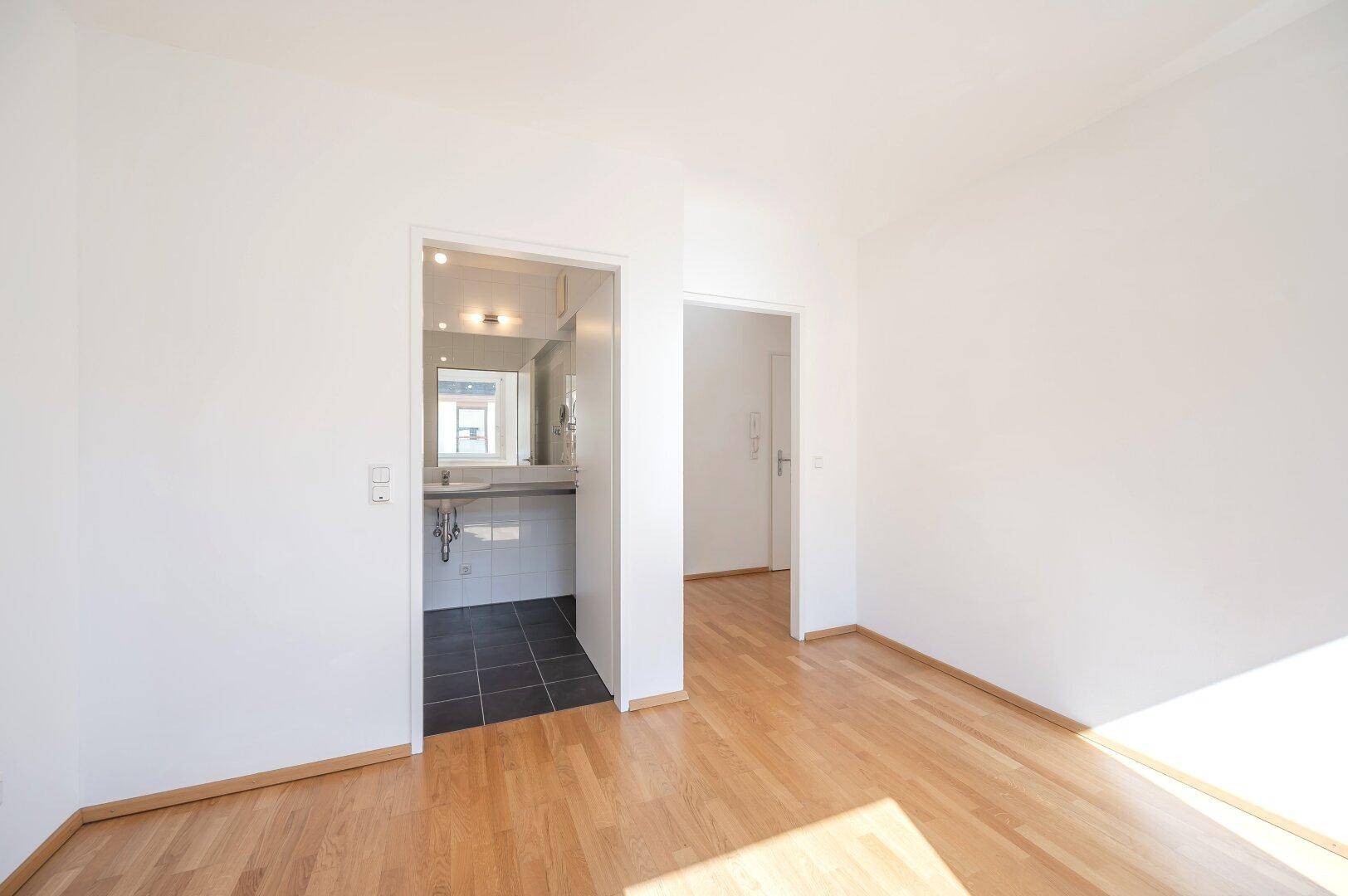 Schlafzimmer mit Parkettboden und direktem Zugang zum Badezimmer, hell und einladend.