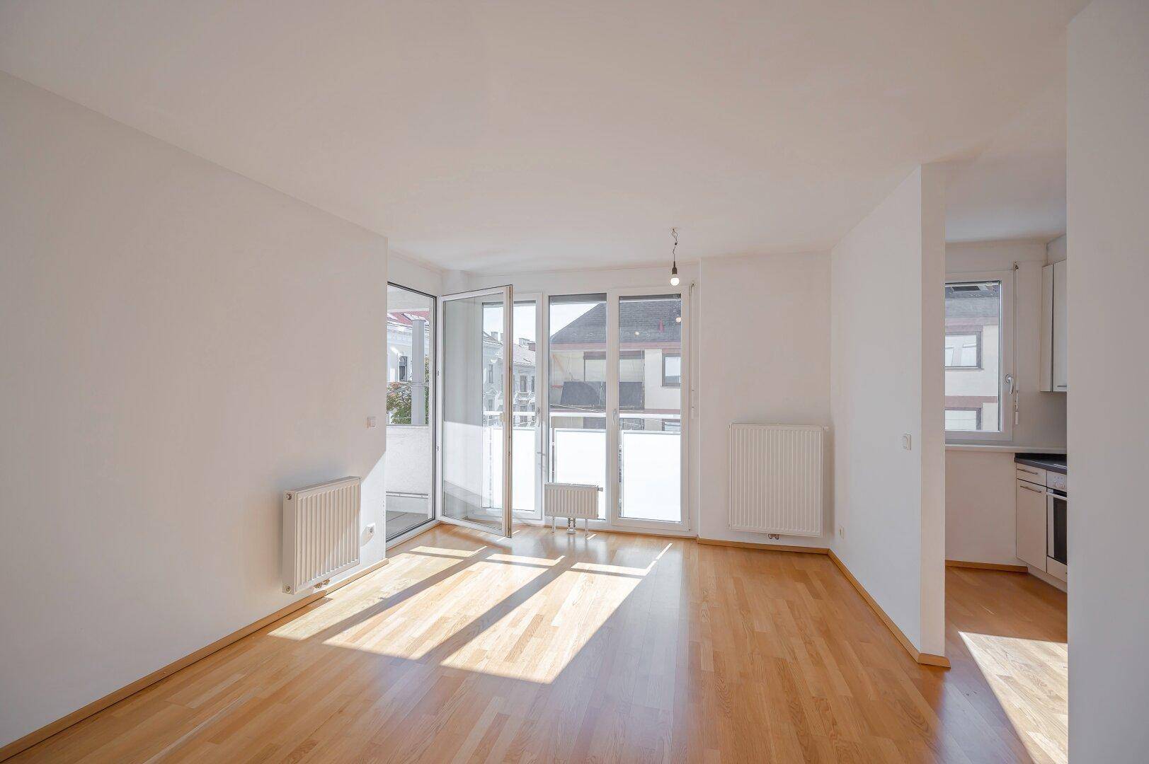 Heller Wohnbereich mit Parkettboden und direktem Zugang zum Balkon, durchflutet von Tageslicht.