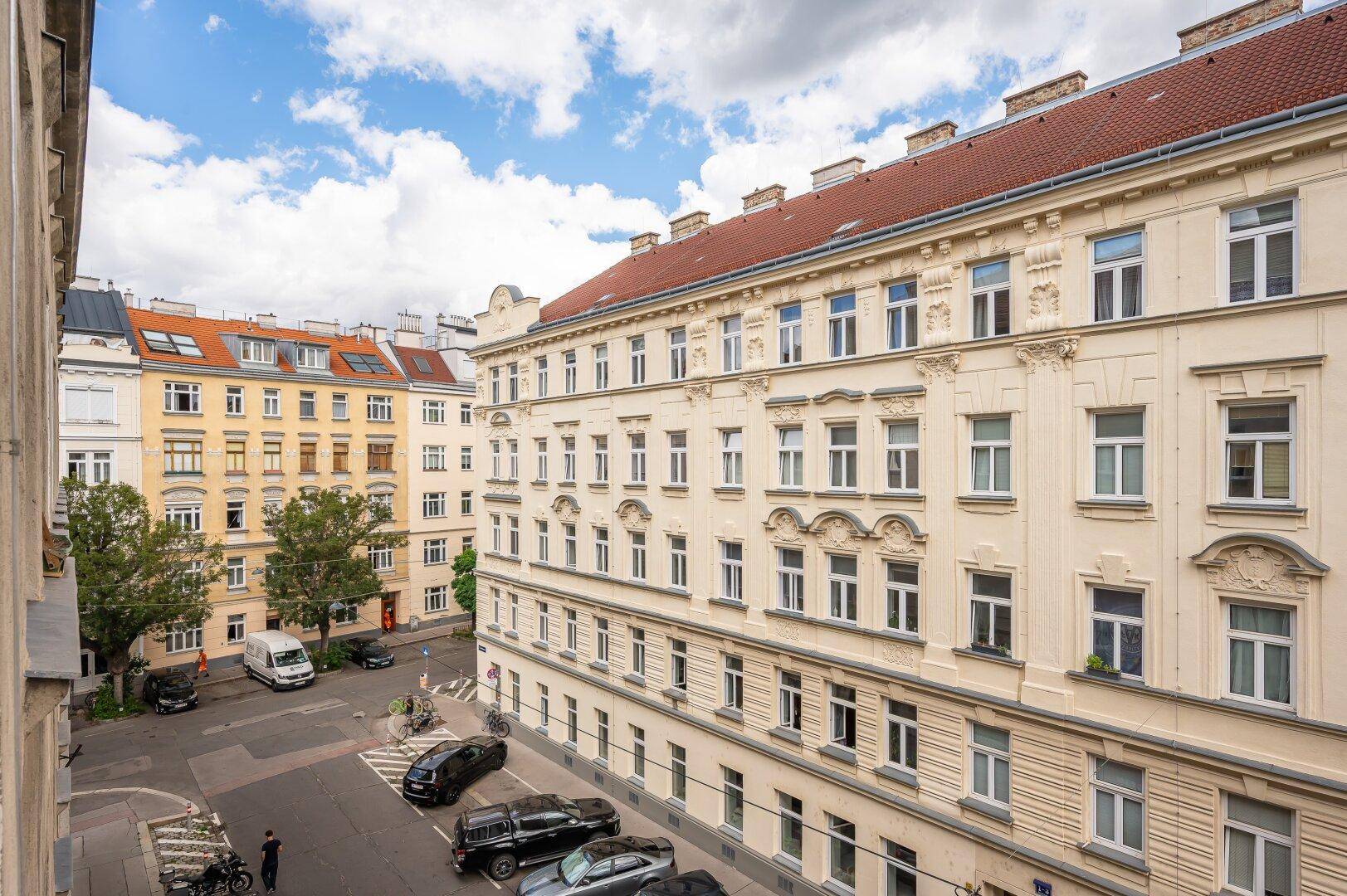 Historische Gebäude entlang einer Straße mit parkenden Autos und blauem Himmel.