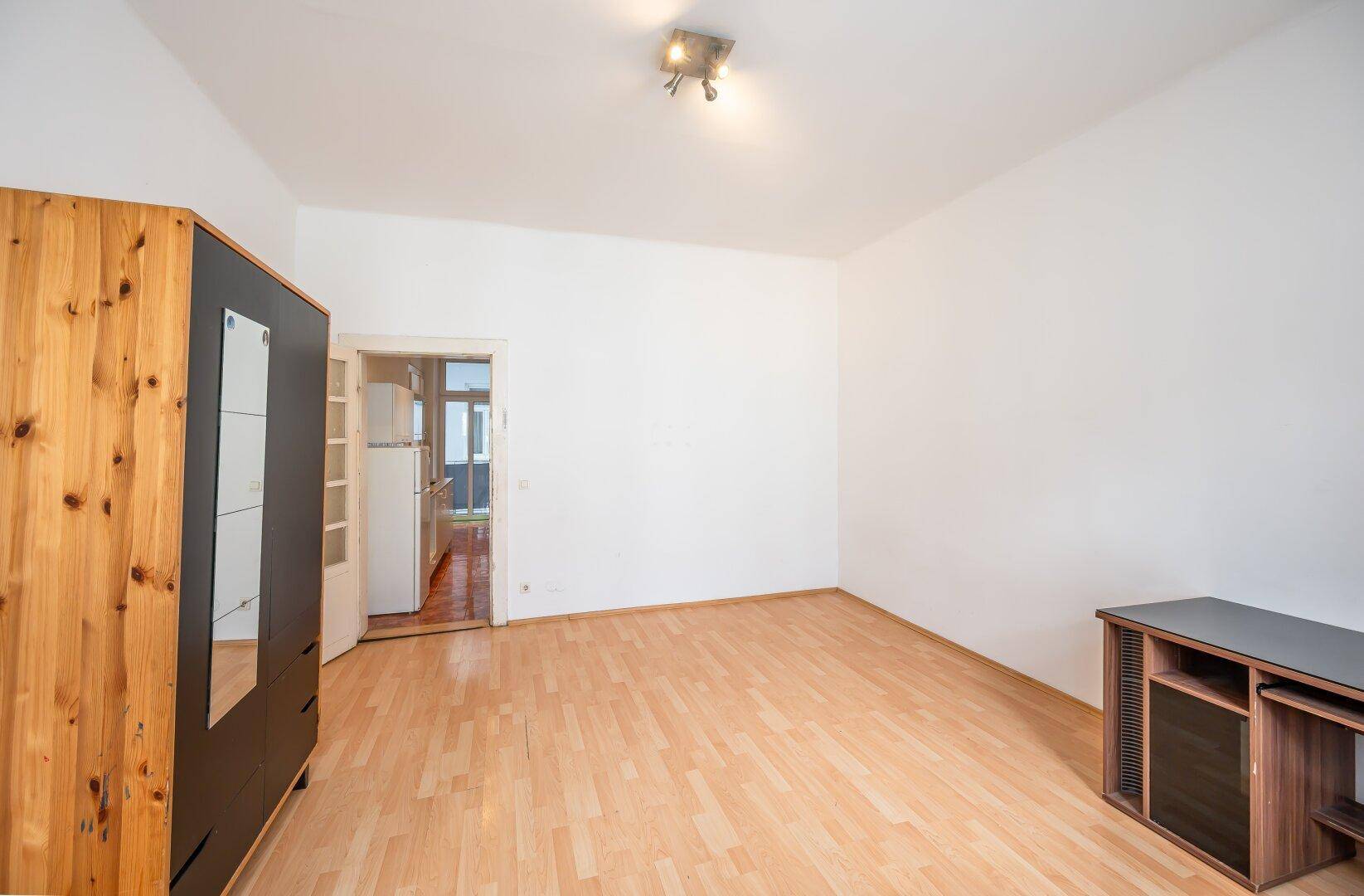 Geräumiges Zimmer mit Holzboden und offenem Zugang zu einer angrenzenden Küche.