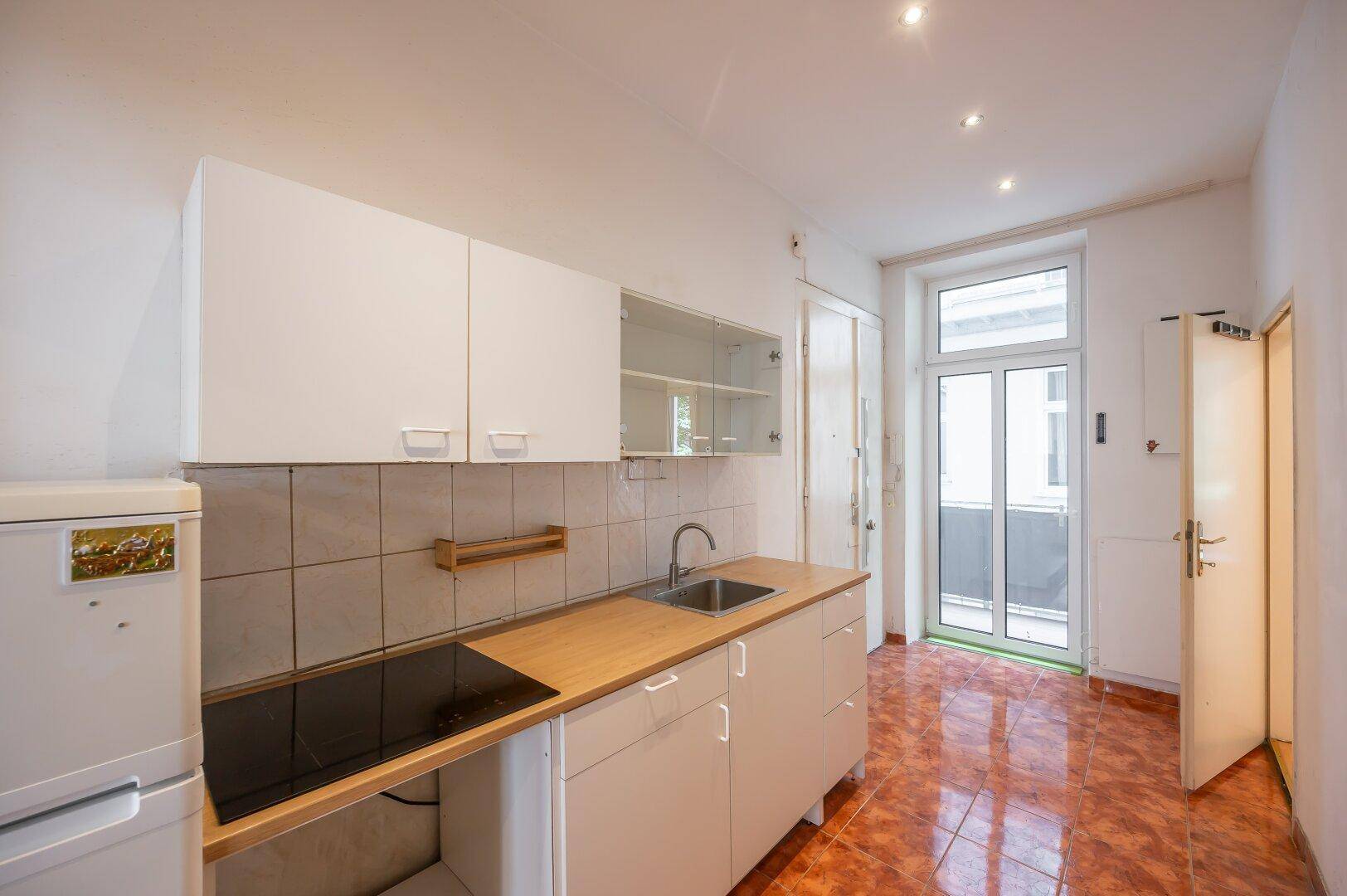 Funktionale Küche mit weißen Schränken, Holztheke und Zugang zum Balkon.