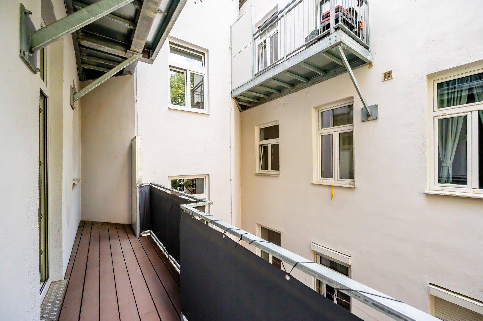 Langer Balkon mit Holzboden und Blick auf die umliegenden Gebäude.