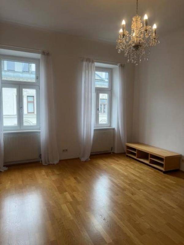 Geräumiges Wohnzimmer mit elegantem Kronleuchter, Parkettboden und viel Tageslicht.