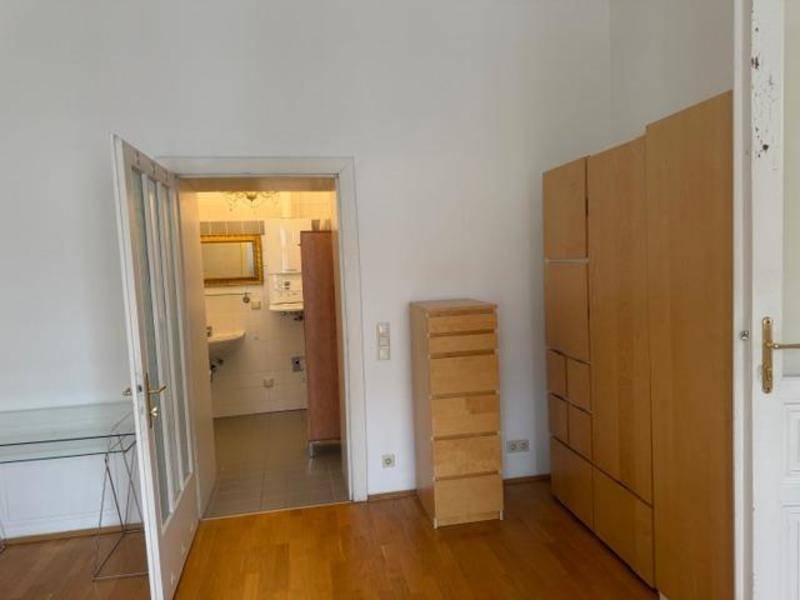 Helles Zimmer mit Parkettboden und Zugang zu einem gefliesten Badezimmer.
