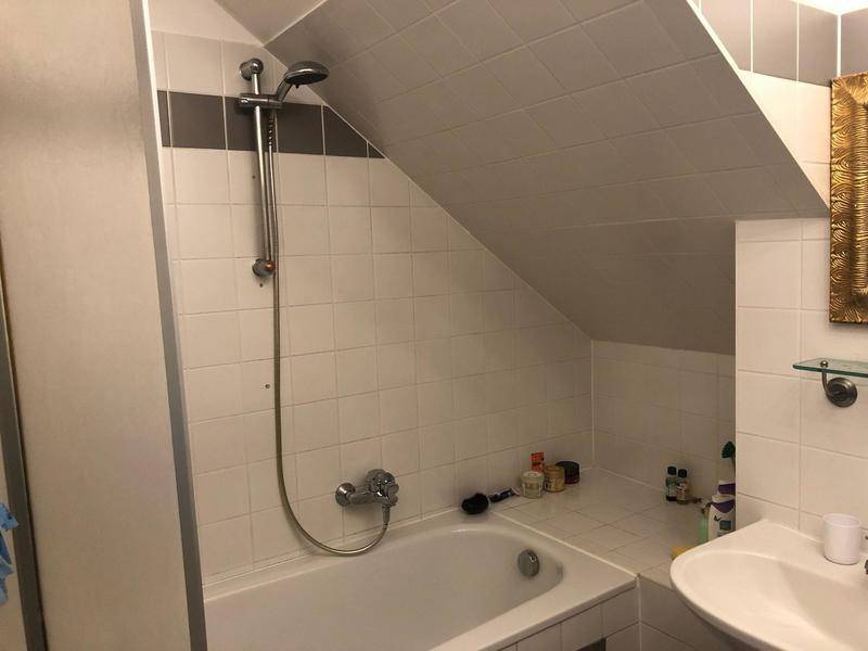 Gefliestes Badezimmer mit Badewanne, Duscharmatur und Waschbecken unter der Dachschräge.