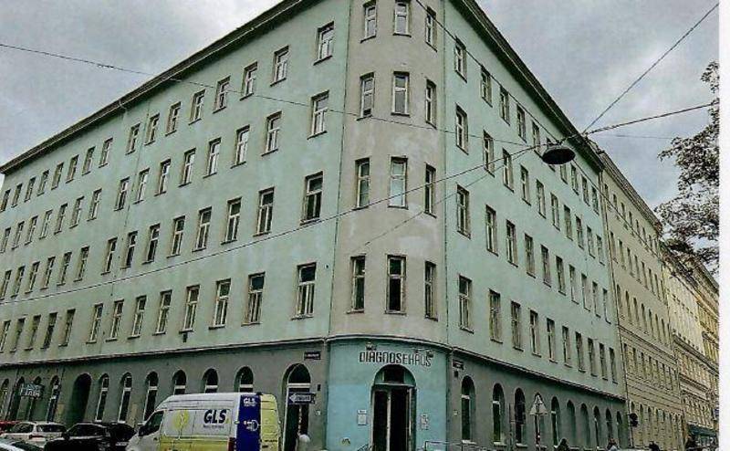 Historisches Eckgebäude mit vielen Fenstern und hellblauer Fassade in urbaner Umgebung.