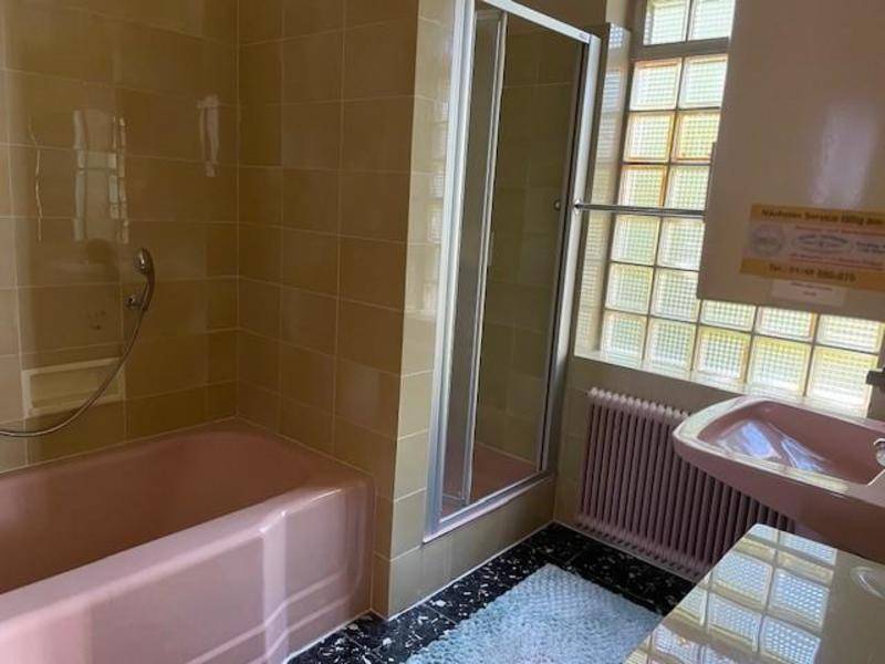 Badezimmer im Stil der 80er Jahre mit rosa Badewanne, Duschkabine und Glasbaustein-Fenster.