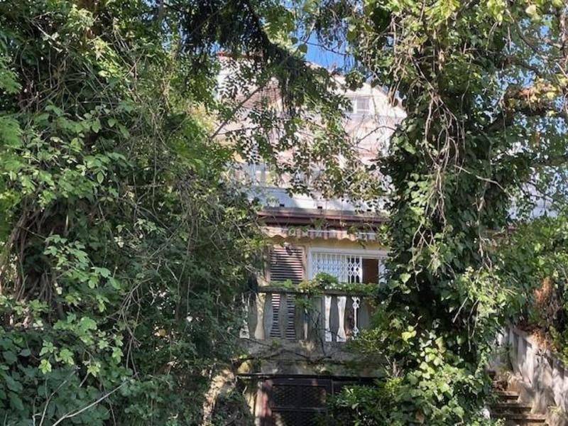 Gebäudeansicht, teilweise von dichtem Laubwerk verdeckt, mit Balkon und Sicherheitsgittern.