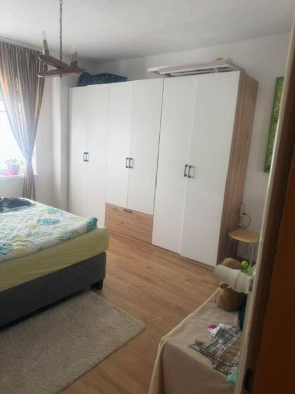 Schlafzimmer mit großem Kleiderschrank, Holzboden und Fenster mit Vorhängen.