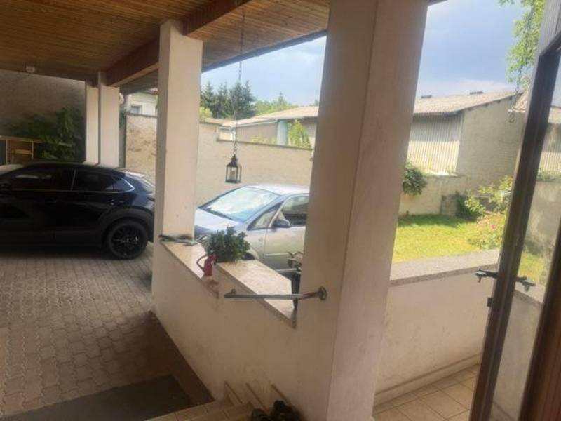 Überdachter Parkplatz mit zwei Autos und Blick auf weitere Gebäude im Hintergrund.
