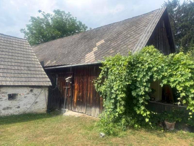 Alte Scheune mit Holzwänden und Ziegeldach, umgeben von üppigem Grün.