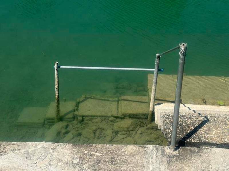 Betontreppe mit Metallgeländer führt direkt in das türkisfarbene Wasser des Kanals.