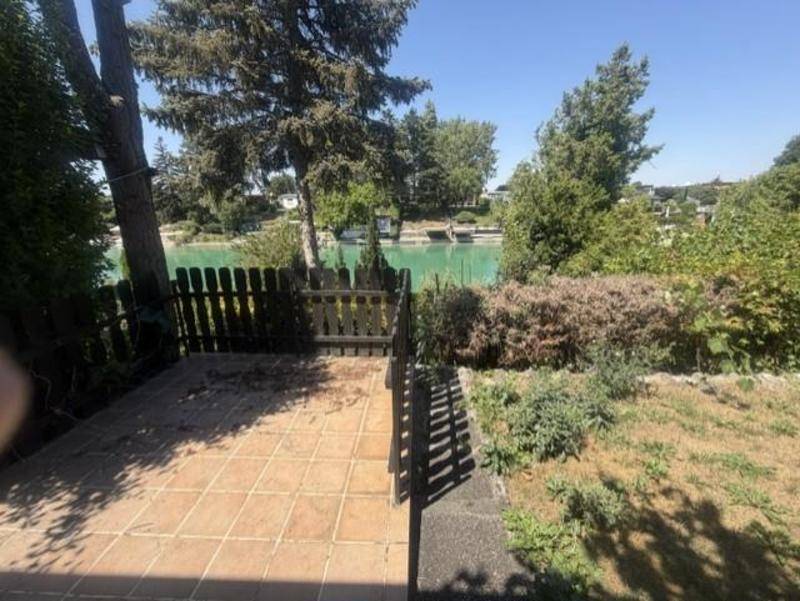 Gepflasterte Terrasse mit Holzzaun und Blick auf den Kanal und die grüne Umgebung.