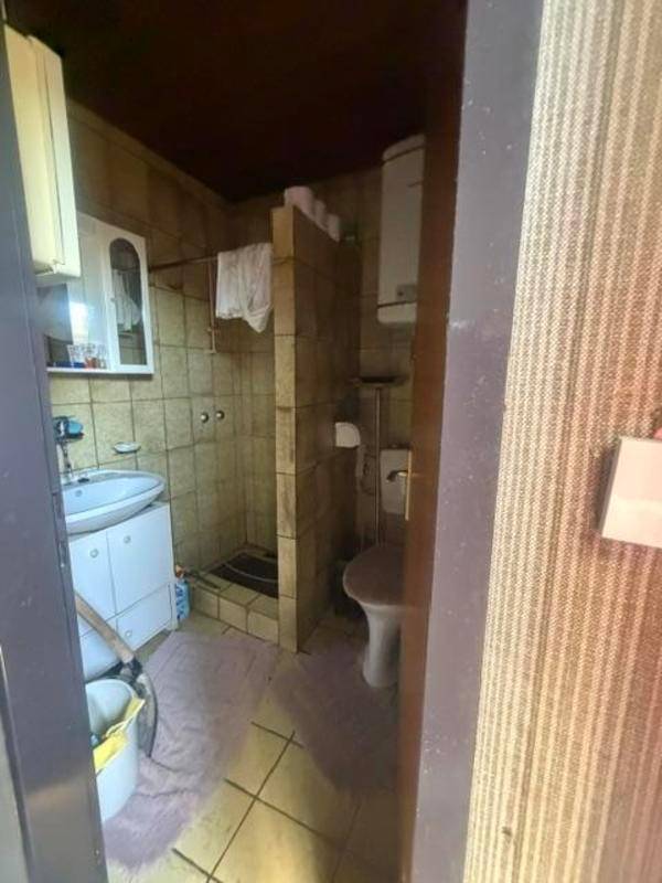 Kleines Badezimmer mit beigefarbenen Fliesen, Dusche und WC in einfacher, funktionaler Ausstattung.