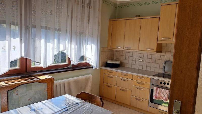 Helle Küche mit Holzschränken, Fenster und Essbereich, bietet Blick ins Grüne.
