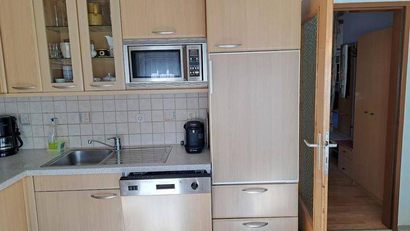 Funktionale Küche mit Holzfronten, Einbaugeräten und Spülmaschine, gut erhalten.