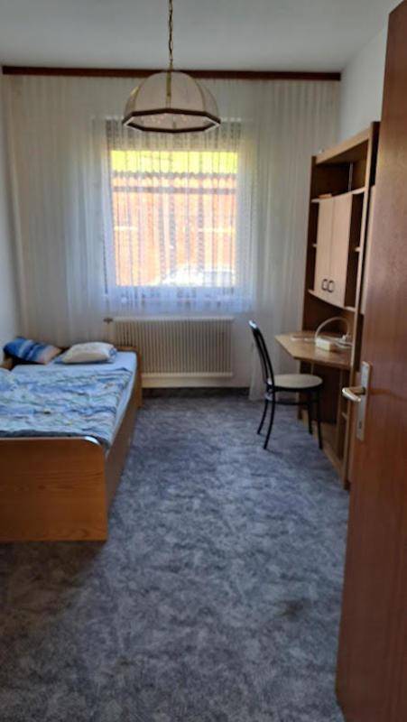 Helles Schlafzimmer mit Einzelbett, Schreibtisch und Teppichboden, ideal für Kinder oder Gäste.