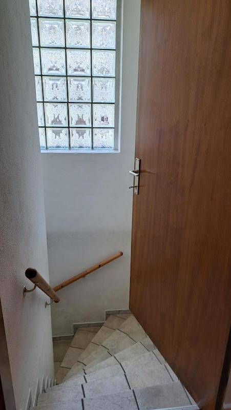 Treppenaufgang mit Holzgeländer und Glasbausteinfenster, das indirektes Licht in den Flur bringt.