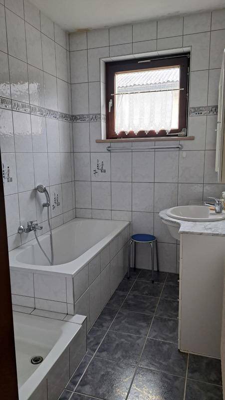 Helles Badezimmer mit Badewanne, Waschbecken und Fenster für natürliche Belüftung, im Stil der 80er Jahre.