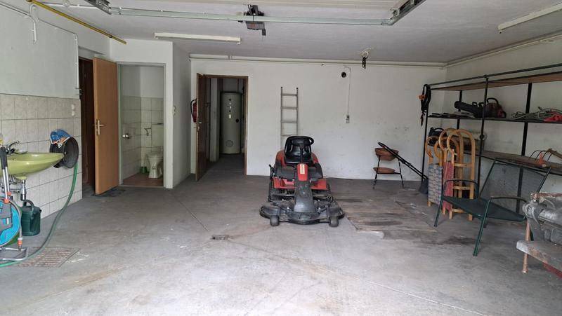 Große Garage mit Betonboden, Werkzeugen und Zugang zu einem separaten WC-Bereich und Waschbecken.