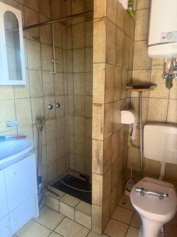 Badezimmer mit gefliester Dusche, Toilette und Waschbecken, in einem älteren Stil gehalten.